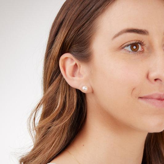 Close-up of a woman wearing akoya ocean pearl and gold earring on a plain background