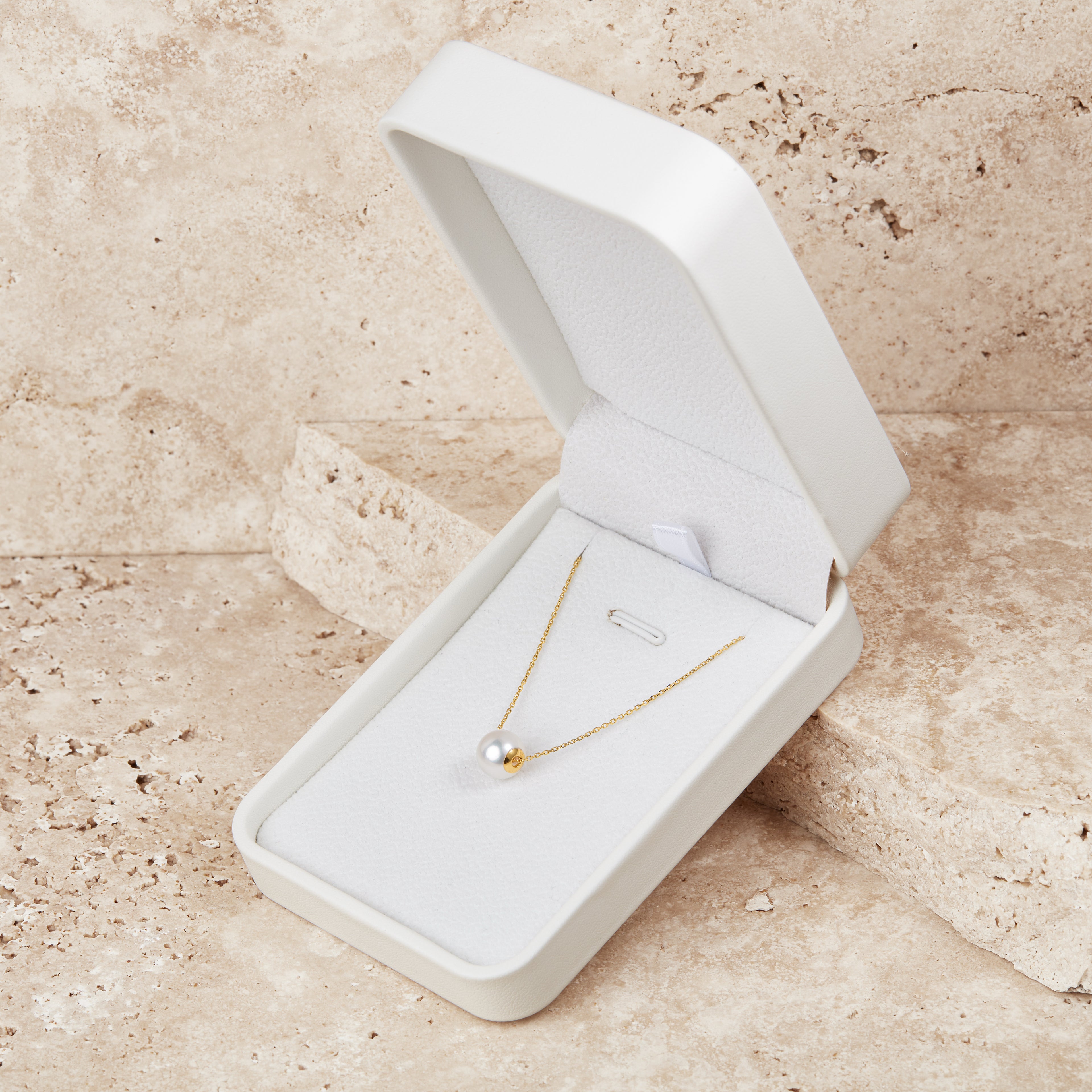 Gold akoya ocean necklace in an open white jewelry box on a beige stone surface