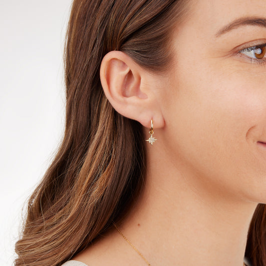 Close-up of a woman wearing a gold hoop earring with a star-shaped diamond studded charm on a plain background