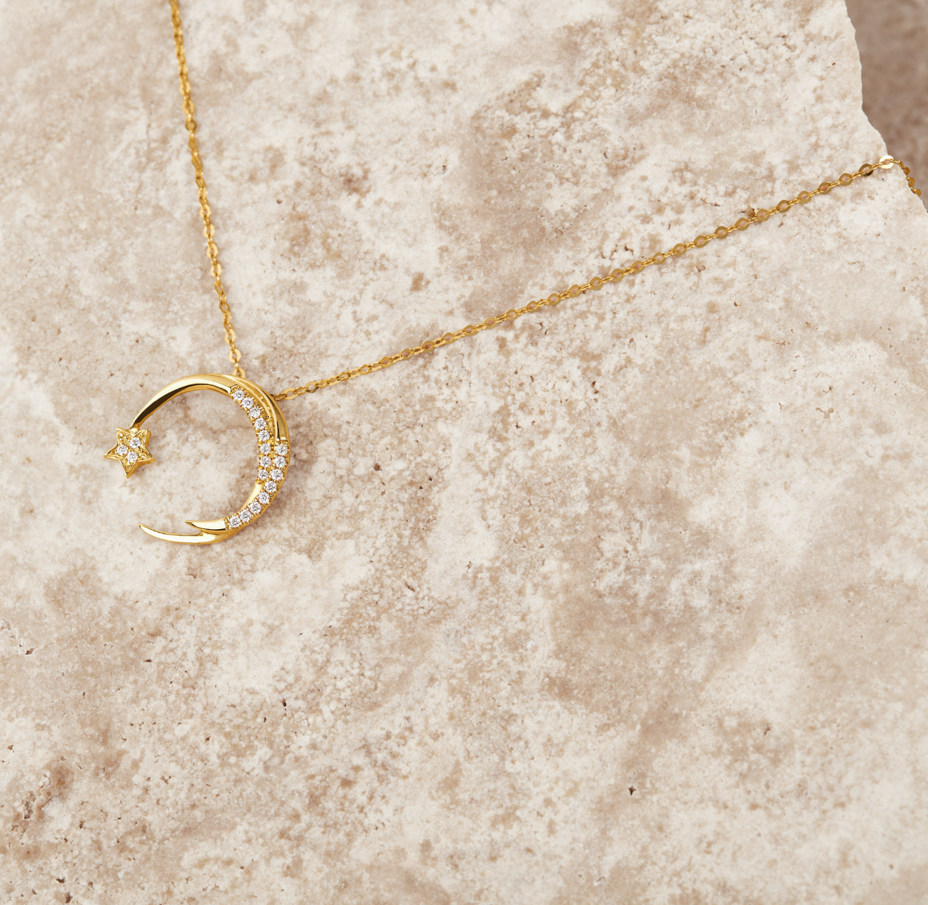 Gold necklace with a falling star diamond studded pendant on a beige stone surface