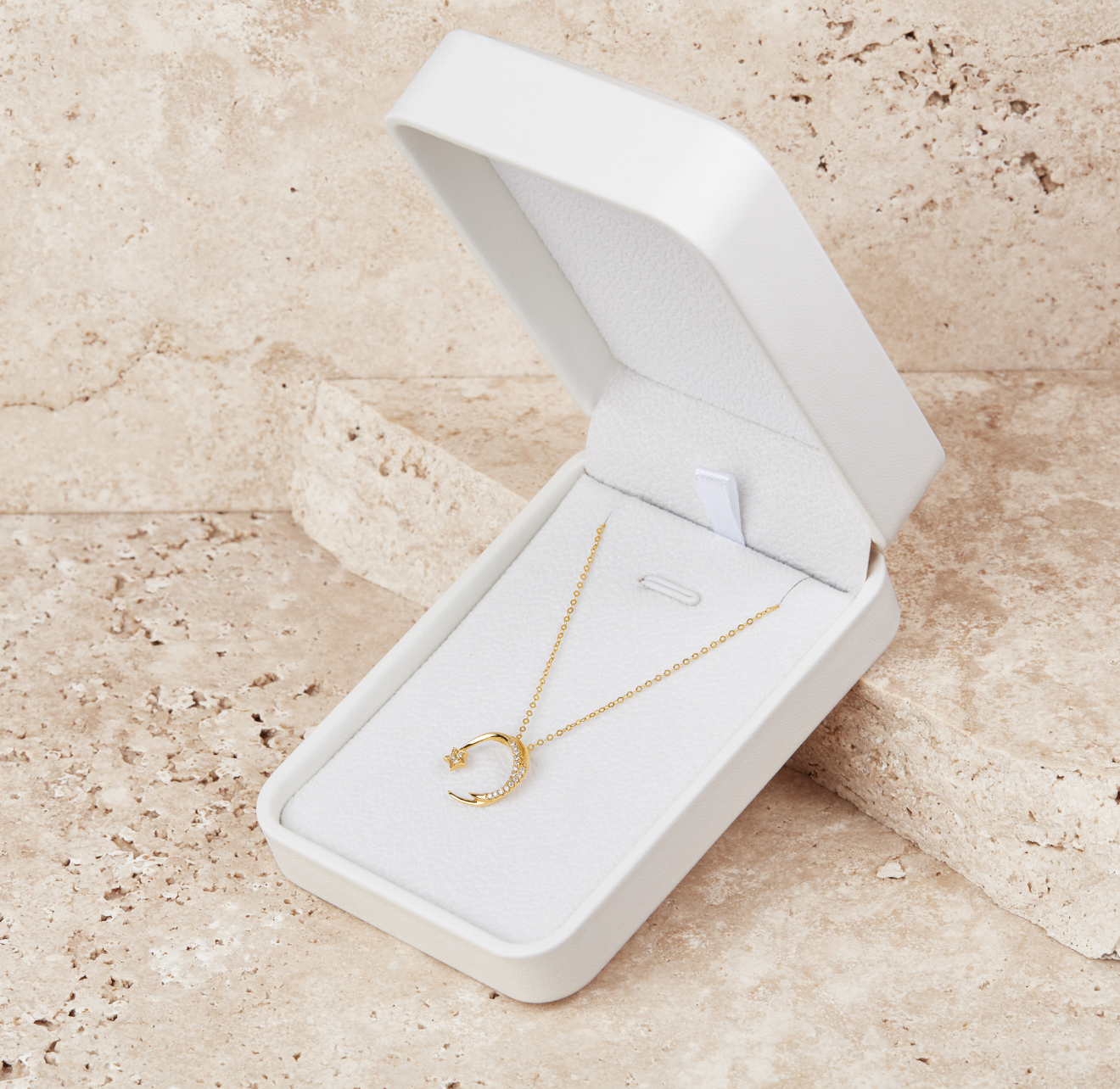 Gold falling star diamond studded pendant on a gold necklace in a white jewelry box on a beige surface