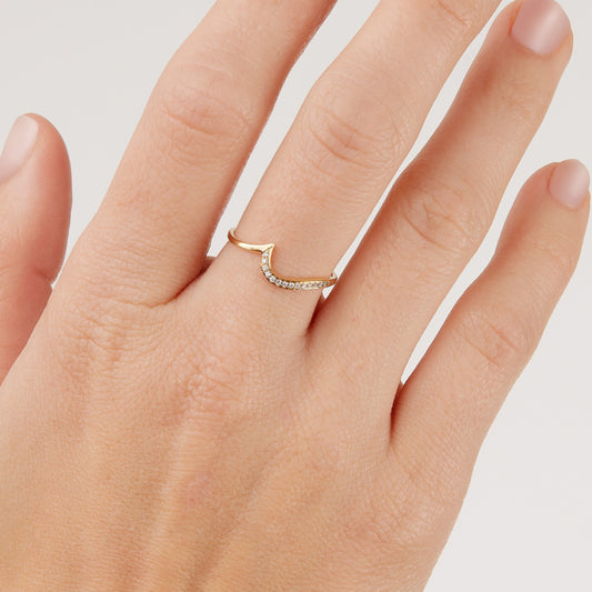 Woman's hand wearing a gold wave shaped ring studded in diamonds on a plain background
